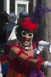 Parade marcher in a feathery costume on a scooter, with a megaphone : Provincetown Carnival parade