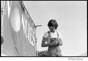 Graham Nash in overalls, standing on stage in front of a No Nukes banner at the No Nukes concert and protest, Washington, D.C.