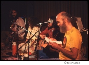 Ram Dass reading from sheet of paper, on stage with Amazing Grace