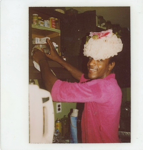 A Photograph of Marsha P. Johnson Wearing a Pink Top and Reaching into a Cabinet