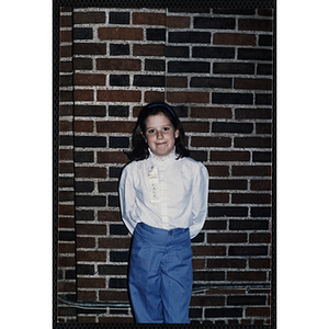 A girl posing against a brick wall with a third place ribbon pinned to her blouse