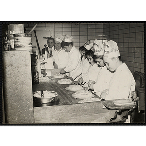 Members of the Tom Pappas Chefs' Club decorate cakes in a Brandeis University kitchen as Director of Dining Halls and Chefs' Club Committee member Norman R. Grimm (far left) and a cook look on
