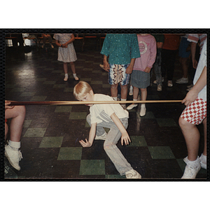 A Boy dancing under a pool cue being used as a limbo stick