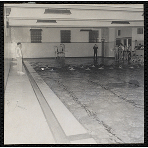 Boys swim in a natorium pool as other boys and two men look on