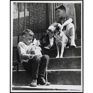 Two boys sitting on the steps, one with a cat and the other with a dog, during a Boys' Club Pet Show