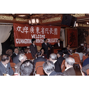 Man speaks to a restaurant full of people gathered to welcome the Guangdong Province delegation