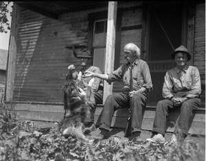 Mr. Kidder, with dog and shotgun, seated on a porch with two other men