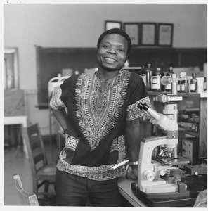 Vincent Saka standing next to microscope in lab