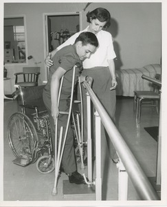 Luis Damilano using parallel bars with assistance from a physical therapist