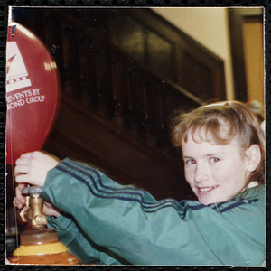 A girl looking at the camera while inflating a balloon with an air tank at a joint Charlestown Boys and Girls Club and Charlestown Against Drugs (CHAD) event