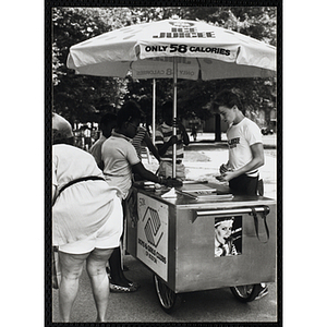 A teenage boy operating an ice juice cart serves customers