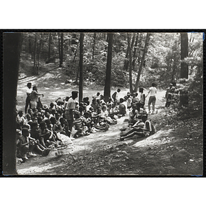 A group of children sit in the woods during an activity