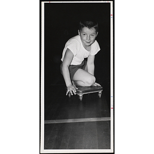 A boy kneels on a scooter in a gymnasium