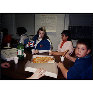 Children sit around a table with pizza and soda at the Tri-Club youth leadership event at the South Boston Clubhouse