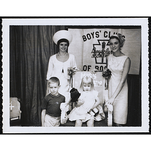 Janet Morrison, Miss Bunker Hill, poses in her throne with a doll, accompanied by her brother and two judges at a Boys' Club Little Sister Contest