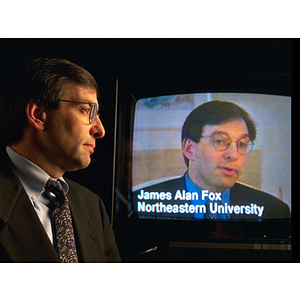 Professor James Alan Fox poses in front of a screen showing his appearance on an unidentified television program