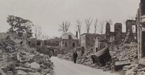 Civilian walking along a town street lined with damaged stone buildings
