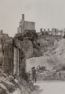 Two men standing on a street corner surounded by badly damaged stone buildings
