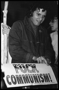 Paul Krassner taping up a sign reading 'Fuck Communism'