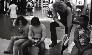 Commune member distributing Free Spirit Press in an indoor shopping mall: communard with group seated in center of the mall