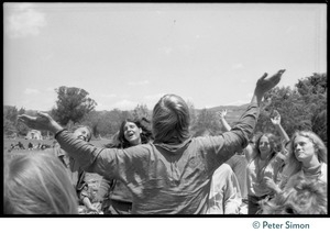 Bhagavan Das raising his arms with a group of dancing women during Ram Dass's appearance at Sonoma State University