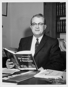 John W. Lederle seated at desk with a copy of Harold Cary's the university of Massachusetts: a history of one hundred years
