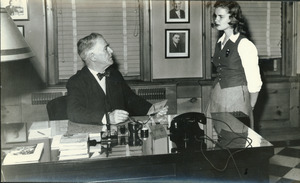 Hugh P. Baker at his office desk and speaking with student