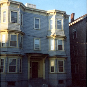 Exterior view of a three-story light blue residential building with yellow trim in Roxbury, Mass