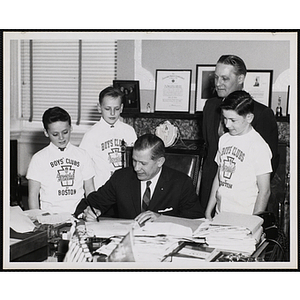 Massachusetts Governor John A. Volpe signs a document while William J. Lynch looks on with three boys in Boys' Clubs of Boston t-shirts