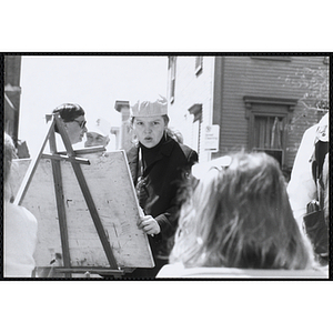 A volunteer artist wearing a hat draws a caricature of a girl at the Boys and Girls Clubs of Boston 100th Anniversary Celebration Street Fair