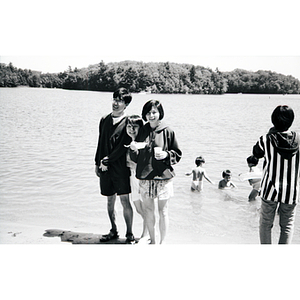 Three young adults stand on a lake shore, smiling