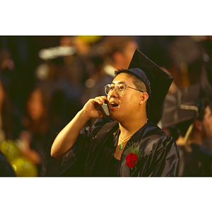 A student in his academic robes and cap on his cell phone during the commencement ceremony