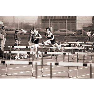 A female Northeastern track athlete jumps a hurtle at a race against Harvard