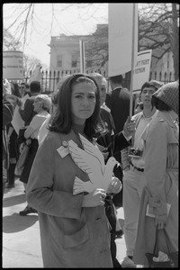 Woman holding a cutout cardboard peace dove and antiwar demonstrators standing in front of the White House during the March on Washington