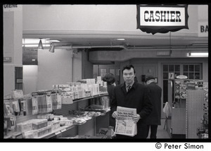 Bill Baird, contraception rights advocate, at a pharmacy, holding up the day's newspaper