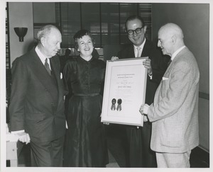 Two men stand holding the 1957 Thumbs Up Award with Jeremiah Milbank and a woman