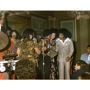 Men and women gathered around microphone with a musical group