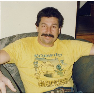 Man in an armchair wearing a yellow t-shirt.