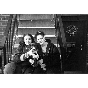 Two teenage girls and a dog sitting on front steps of a Villa Victoria row house.
