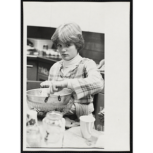 A girls uses a colander and a bowl in a kitchen