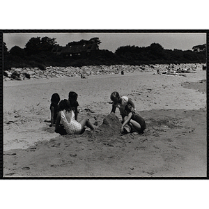 Five girls play with sand on a beach