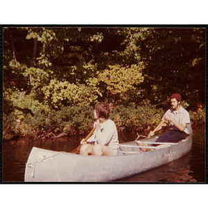 Two teenagers paddle a canoe