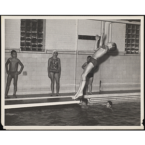 A boy executes a dive from a diving board in a natatorium pool