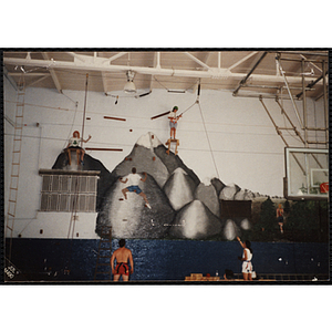 An indoor climbing supervisor holds a safety rope for a girl on a platform