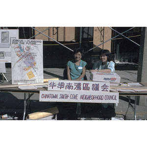 Suzanne Lee sits with another woman at the Chinatown South Cove Neighborhood Council table during the August Moon Festival in Boston's Chinatown