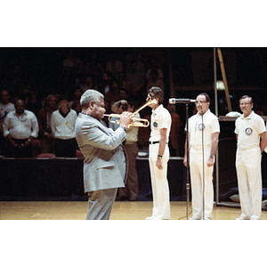 Man plays the trumpet on a volleyball court, while three men stand in a line behind him