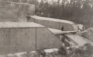 Close-up of a large German gun turret in a circular concrete enclosure with two men standing next to it for scale