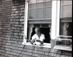 May Webster, leaning through a window, feeding a hummingbird by hand