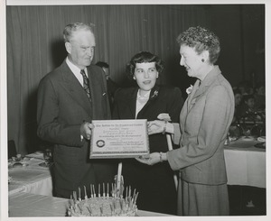Bruce Barton presents a certificate in front of a woman on crutches at the Institute for the Crippled and Disabled's 35th anniversary Red Cross luncheon