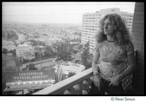 Robert Plant looking out from the balcony of his room at the Riot House, a billboard advertising Led Zeppelin's new album Physical Graffiti in the background